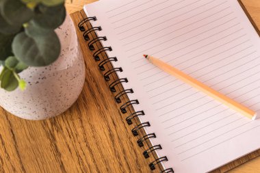 Beyaz sayfaları ve kahverengi ahşap yay kaplı kapağı olan açık bir not defteri masanın üzerinde bir bulut ya da kalemin yanında duruyor. Yukarıdan görüntüle