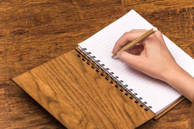 Bir adam açık bir not defterine beyaz sayfalar ve masanın üzerinde duran ahşap kahverengi bir kapakla yazar.