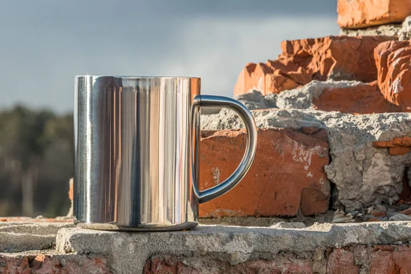 A stainless steel cup for drinks stands on a brick wall against a blue sky background
