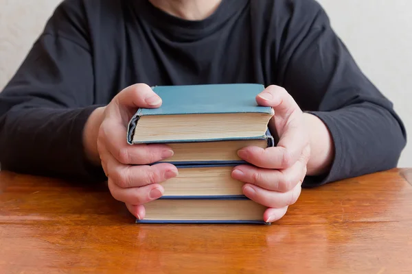 Donna seduta a tavola e tiene una pila di vecchi libri — Foto Stock