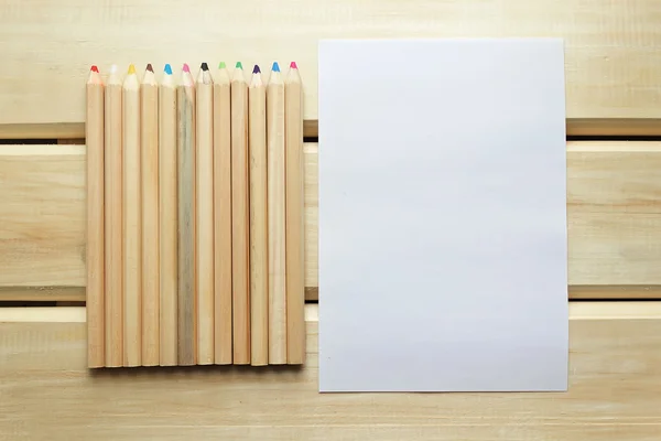 Lápices de colores y papel en blanco sobre una superficie de madera — Foto de Stock