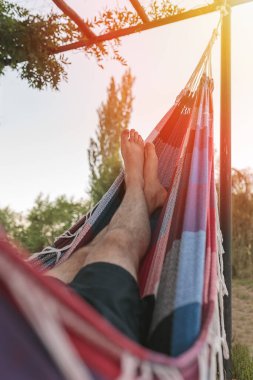 Bir adam gün batımında yeşil bir bahçede hamakta kestiriyor. Yazın doğada dışarıda uyukluyorlar..
