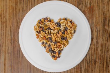 Beyaz bir tabakta, kalp şeklinde gruplanmış çeşitli fındıkların üst görüntüsü. Badem, ceviz, fındık, fıstık..