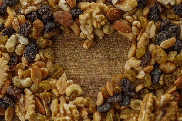 A macro photography of mix nuts. Raisins and a variety of dried fruits, grouped together forming a heart on a wood texture. Almonds, walnuts, hazelnuts, cashew, peanuts.