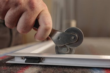 Tekerlekli bir aletle alüminyum sivrisinek ekranı takan bir adam eli. Yatay resim.