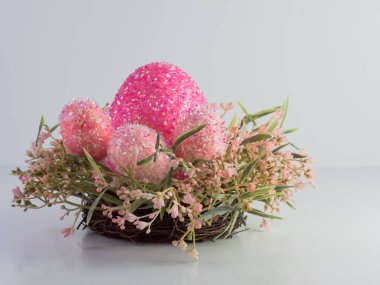 Pembe boncuklu Paskalya yumurtaları pembe ve yeşil çiçekli bir çelengin içinde beyaz arka planda duruyor. Tatil dekorasyonu.