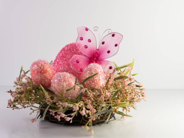 Pembe kelebek pembe bir Paskalya yumurtasının içinde, pembe bir bahar çelenginde beyaz arka planda daha küçük pembe yumurtalarla oturuyor. Bahar ve tatil dekoru.