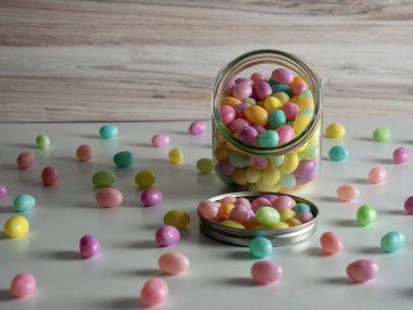 Paskalya jelibonları şeker kavanozundan beyaz bir tezgaha dökülüyor. Pastel renkler, şeker, şenlikli ve lezzetli!