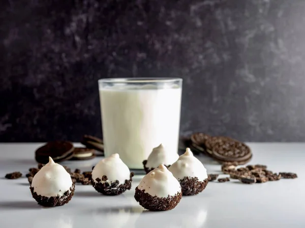 Cookies and Cream cake balls, truffle like dessert, with a fresh glass of milk and sandwich cookies in the background, on a white counter with a black marbled wall.  Food still life photography.