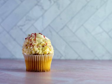 Üstünde kırmızı ahududu çiseleyen kıvrımlı beyaz çikolatalı beyaz kek pembe mermer tezgahlı lezzetli tatlı ve ringa kemikli fayans duvarı..