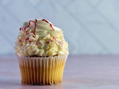 Üstünde kırmızı ahududu çiseleyen kıvrımlı beyaz çikolatalı beyaz kek pembe mermer tezgahlı lezzetli tatlı ve ringa kemikli fayans duvarı..