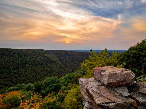 Overlook of the mountains and the fall foliage at Coopers Rock State Forest in West Virginia with the sunset golden sky one direction and a blue swirly sky the other direction, with the rock cliff.