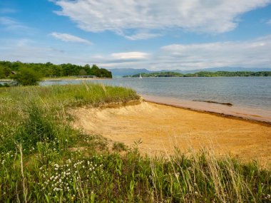 Douglas Gölü ilkbaharda Tennessee 'de. Arka planda Büyük Smoky Dağları, su ve kumlu kıyılar. Uzakta bulutlarla dolu mavi bir gökyüzü..  