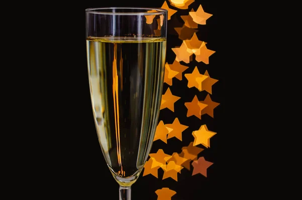 暗い背景に金色の星形のボケライトと輝くワインのガラスの焦点 — ストック写真