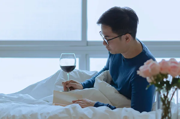 A person reading book on bed with a glass of red wine. Digital detox and social disconnect concept.