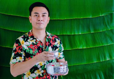 Elinde muz yaprağı arkaplanlı Songkran festivali için çiçek taşıyan Taylandlı bir adam..