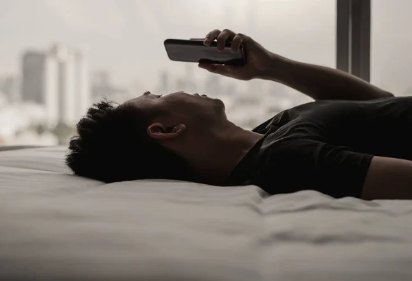 Asian man feels sad on bed looking and focus on smartphone. Internet social media addiction and mental health concept.