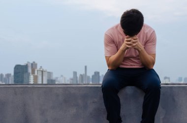 Asian miserable depressed man sit alone with city background. Depression and mental health concept.