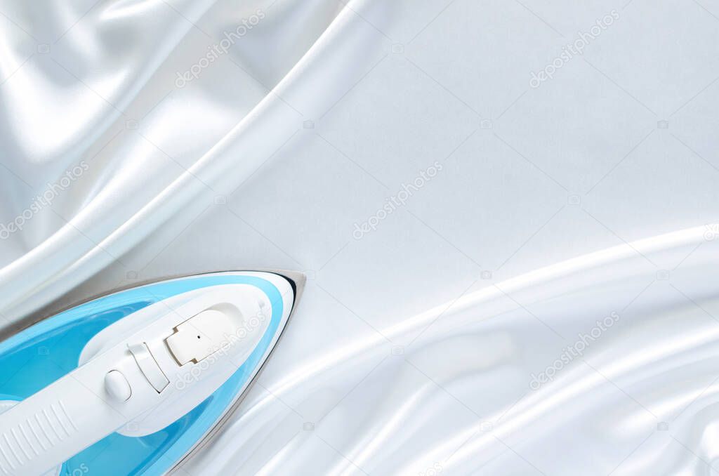 Electric iron on smooth and wavy white cloth texture with space for text. Housekeeping concept.