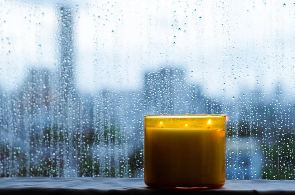 モンスーンの季節に雨が降る窓のそばに置かれた香りのろうそくを燃やす 禅とリラックスの概念 — ストック写真