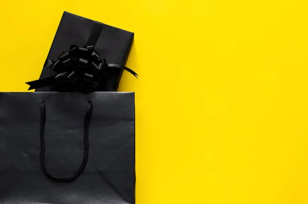 A black gift box puts in black shopping bag with yellow background. Black friday and Boxing day concept.