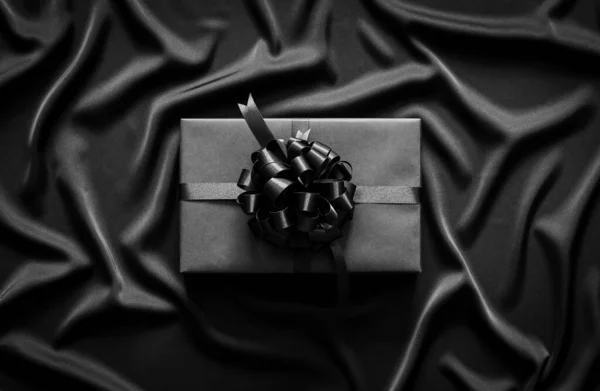 一个有缎带的黑色礼品盒 放在黑色波浪布上 黑色星期五及节礼日概念 — 图库照片