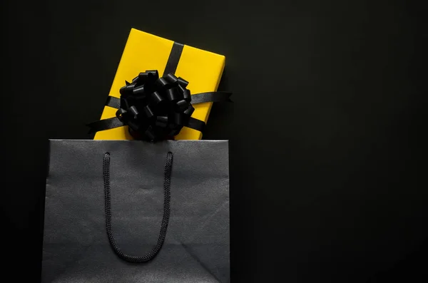 A yellow gift box puts in black shopping bag with black background. Black friday and Boxing day concept.