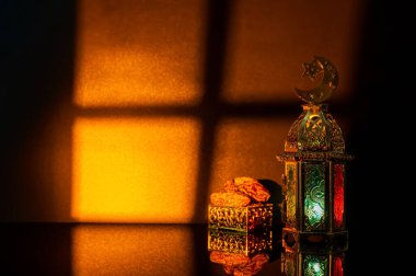 Süslü altın bir fener ve dekoratif bir kutu pencereden gelen sıcak günbatımı ışığı altında parlıyor..