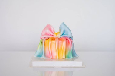 Renkli gökkuşağı hediye pastası, beyaz arka planda geniş kumaştan bir fiyonk..