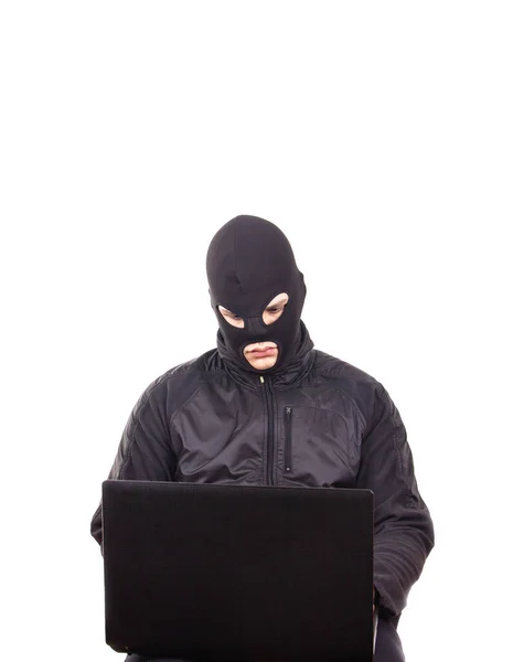 Siyah maskeli, cep telefonu ve dizüstü bilgisayarı olan bir adam internet dolandırıcılığıyla meşgul.