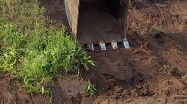 Kazıcı bir kovayla toprağı kazıyor.