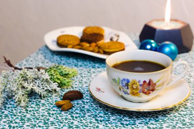 Mavi arka planda bir fincan kahve, mum, kurabiye ve Noel süslemeleri.