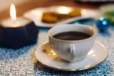 Mavi arka planda bir fincan kahve, mum, kurabiye ve Noel süslemeleri.