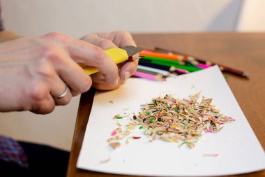 Bir adam kırtasiye bıçağıyla bir kalemi keskinleştirir.