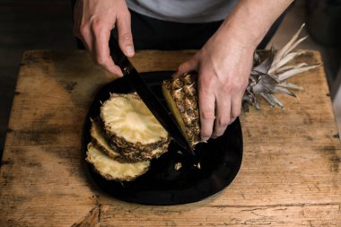 Adam ananası tahta bir masada bıçakla kesiyor.