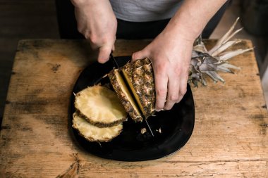 Adam ananası tahta bir masada bıçakla kesiyor.