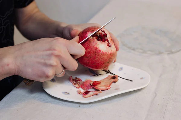 Чоловік очищає гранатовий фрукт ножем на тарілці — стокове фото
