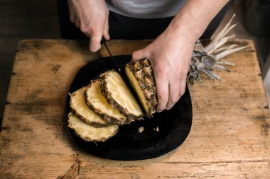 Adam ananası tahta bir masada bıçakla kesiyor.