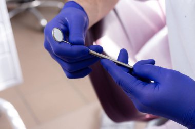 Mavi tıbbi eldivenli erkek ellerinde diş aynası.