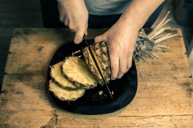 Adam ananası tahta bir masada bıçakla kesiyor.