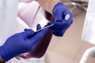 Mavi tıbbi eldivenli erkek ellerinde diş aynası.