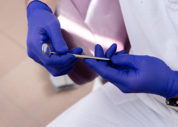 Dental mirror in male hands with blue medical gloves