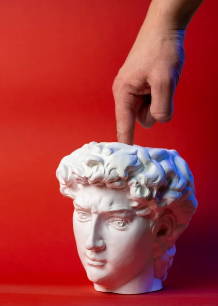Pote de gesso na forma de cabeça Davids e mão masculina em um fundo vermelho. — Fotografia de Stock