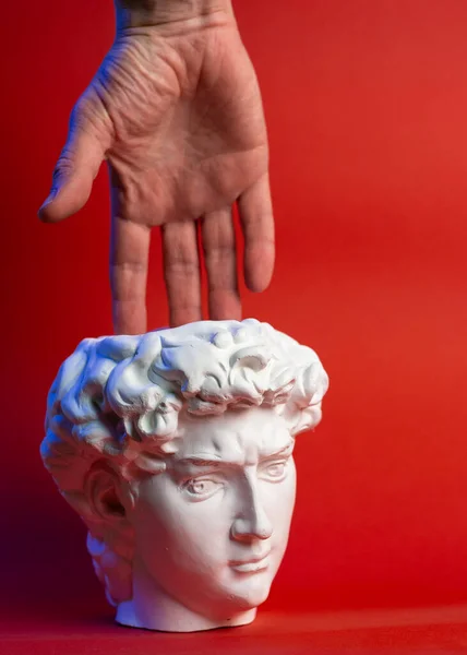 赤い背景にデビッドの頭と男性の手の形の石膏鍋. — ストック写真