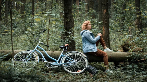 Femme avec vélo bleu assis sur un arbre tombé dans la forêt — Photo