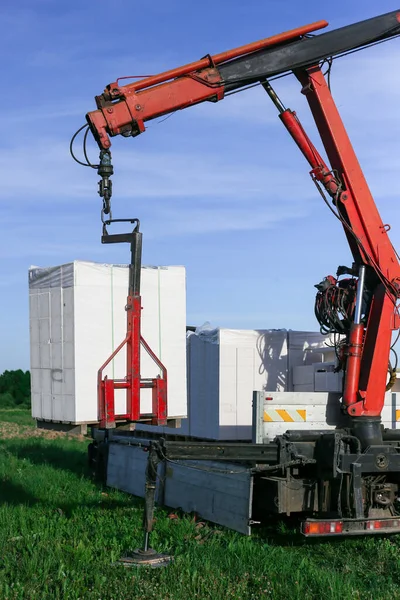 Het lossen van bouwstenen uit een vrachtwagen met behulp van een kraan. Hydraulische manipulator. Stockfoto