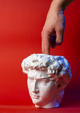 David kafası şeklinde alçı kap ve erkek eli kırmızı arka planda..