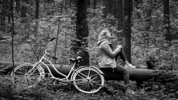 Vrouw met fiets zittend op een omgevallen boom in het bos. Zwart en whait foto. — Stockfoto