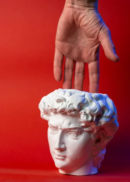 Plaster pot in the form of Davids head and male hand on a red background. — Stock Photo, Image