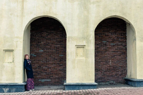 Une femme blonde en manteau noir se tient sous une arche — Photo